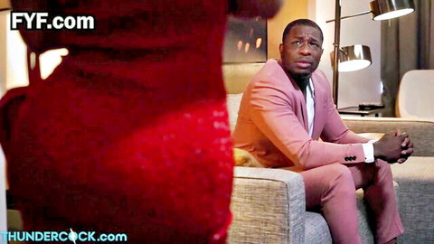 Black stud in pink suit sits on couch eyeing woman's red dress bubble butt