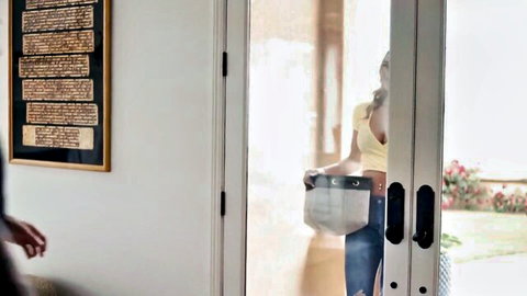 Blonde babe with deep cleavage in yellow top and tight jeans grabbed by man's hand on hip by glass door