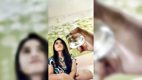 Cute Asian teen in colorful top looking up at hand holding glass of clear liquid