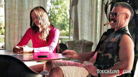 Skinny brunette teen in pink top sits at table with rough biker guy smoking cigar reaching hand out