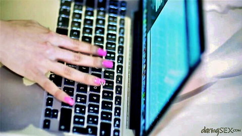 Closeup of woman's hand with long pink nails typing on laptop keyboard seductively