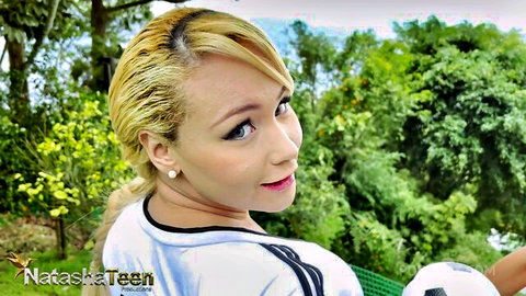 Cute blonde Asian teen in tight soccer jersey teasing playfully outdoors with soccer ball