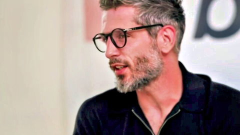 Handsome mature man with gray beard glasses smirking in black zipped polo shirt