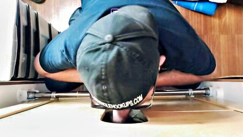 Man in cap kneeling at glory hole, tugging pants for blowjob tease