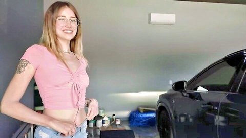 Blonde teen with glasses smiles while unbuttoning tiny frayed shorts exposing bush in garage next to Tesla