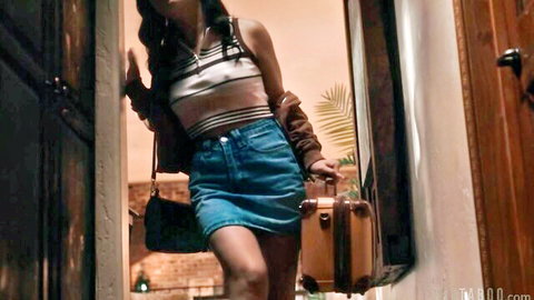 Petite Asian brunette in striped tank top and denim miniskirt holding suitcase in doorway