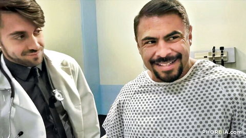 Handsome doctor in white coat smiles at bearded patient in hospital gown during exam
