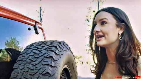 Sexy smiling brunette showing deep cleavage next to massive Jeep tire outdoors