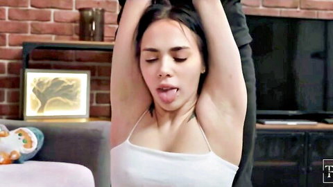 Brunette beauty sticks out tongue, arms raised in white tank top, teasing pose