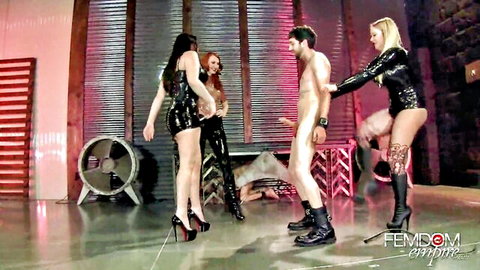 Three latex dominatrixes ballbusting nude male slave in femdom scene
