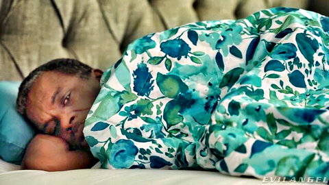Richard Mann resting nude under floral blanket in bed