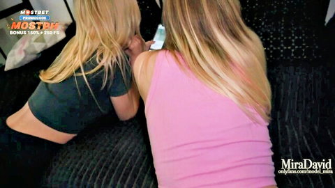 Blonde teens Mira David and Lis Evans in tank tops lounging on couch
