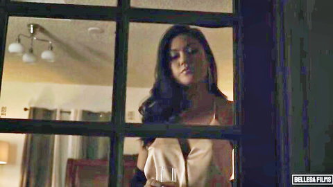 Kendra Spade in seductive yellow slip dress, gazing out window with wine glass