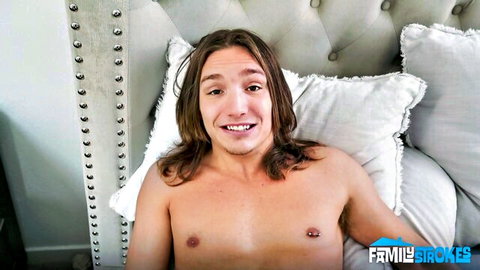 Smiling young man with long hair lying shirtless in bed for morning wake-up surprise