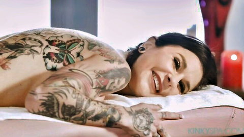 Inked MILF lying nude, smiling with butterfly tattoos on back