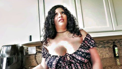 Curvy ebony woman in low-cut floral dress teasing cleavage in kitchen