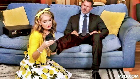Blonde MILF in yellow dress holds high heel for suited man on couch tease