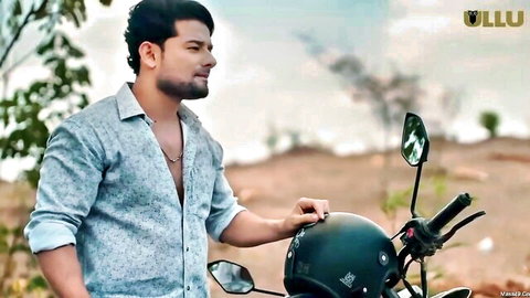 Handsome bearded Indian man in open shirt leaning on motorcycle with black helmet outdoors