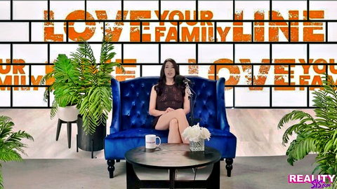 Alex Coal in burgundy dress on couch, teasing family line theme