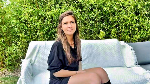 Brunette European saleswoman in black dress and stockings sits smiling outdoors