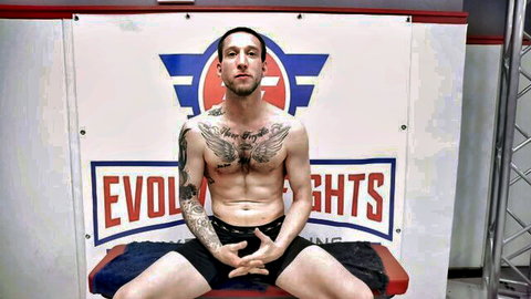 Tattooed muscular man spreads legs showing bulge in tight shorts at Evol Fights event