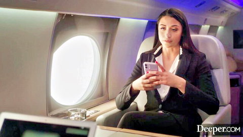 Angela White in seductive business attire on a private jet, looking at phone