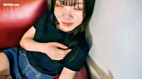 Cute Japanese girl with bangs smiling playfully in black top and denim shorts on red couch