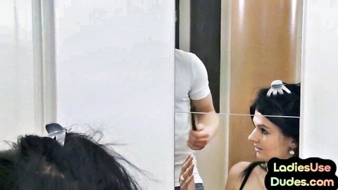Femdom mistress with black hair smiles in mirror as muscular dude holds her ponytail in store