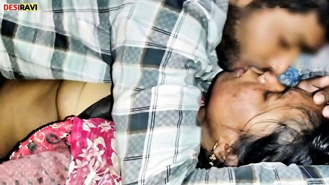 Bearded Indian man passionately kissing young woman's neck as she lies in pink saree exposing bare midriff on bed