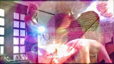 Pink-haired woman holds glowing blue orb over naked man's exposed bare ass in mystical purple-lit room