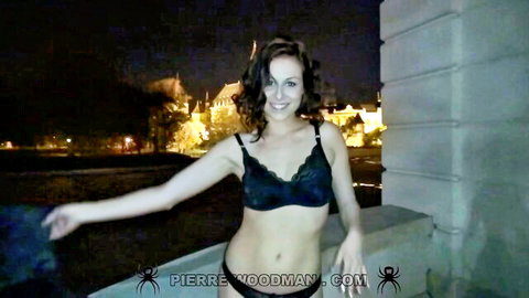 Young brunette in black lace bra poses seductively on nighttime balcony with city lights