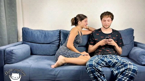 Horny stepsister in short dress leans over stepbrother on couch, teasing him