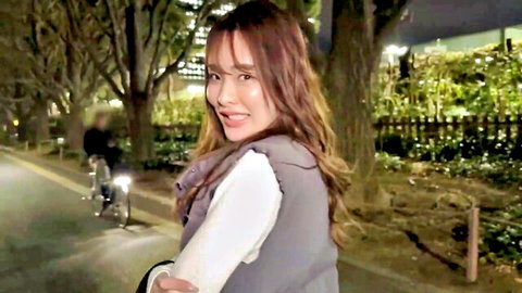 Smiling Asian gal in vest and white top walking in nighttime park, JAV style