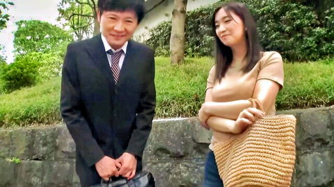 Japanese suited man smiling at sexy Asian woman in beige top and skirt outdoors