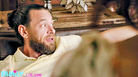 Bearded brunette man with man bun smirks in yellow shirt on couch in porn scene