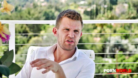 Bridgette B's male co-star gesturing intensely on balcony in anal scene preview