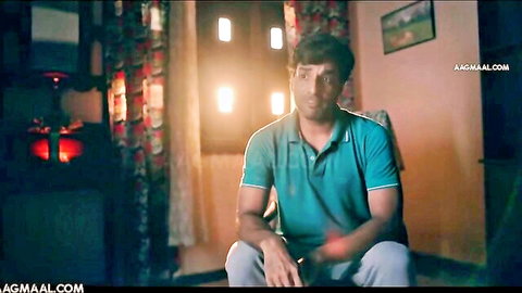 South Asian man in teal polo shirt sitting casually with legs apart in warmly lit room