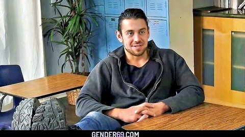 Young brunette guy in hoodie smiling at desk in school classroom