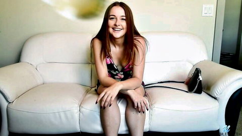 Smiling petite redhead teen babe with small tits spreading legs in pink dress on couch