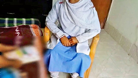 Clothed South Asian woman in white salwar kameez and blue dupatta sitting demurely on wooden chair