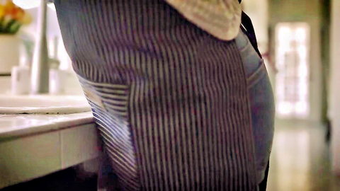 Charlie Forde in apron bending over sink, teasing curvy ass