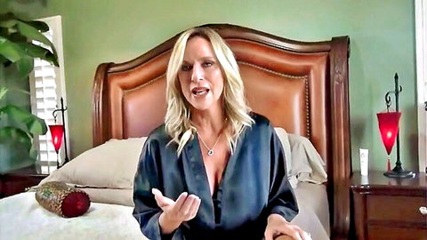 Blonde MILF in deep cleavage satin robe gesturing seductively on bed