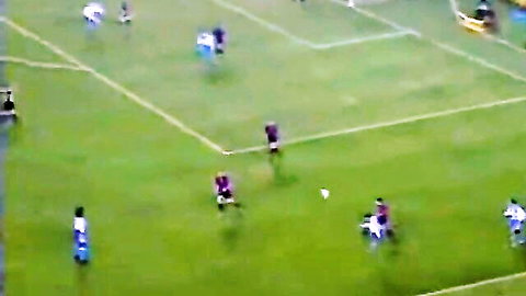 Aerial view of soccer players in blue and maroon jerseys chasing ball on green field