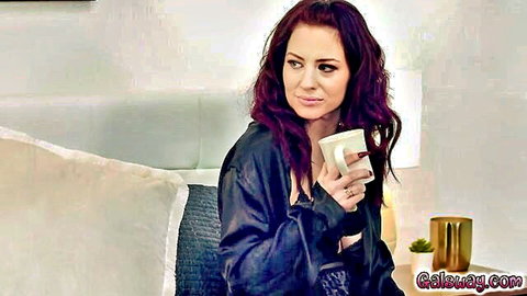 Jessica in seductive black satin robe, red hair, holding mug on bed