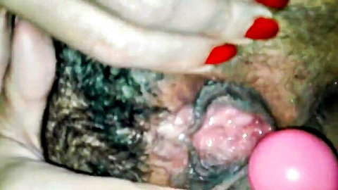 Hairy pussy spread wide by red-nailed fingers with pink toy ball inserted inside
