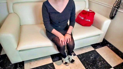 Asian woman in black dress and stockings sitting on couch