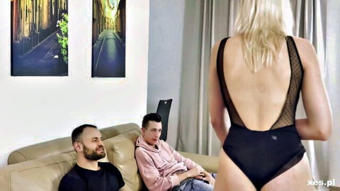 Blonde in black lace bodysuit teases two men on couch, adrenaline thrill