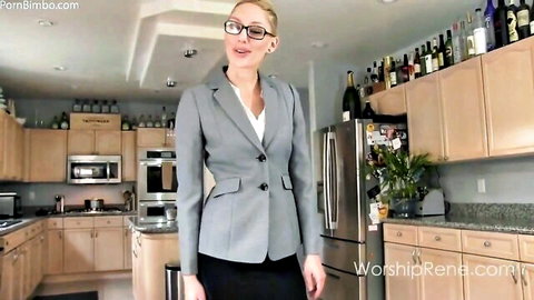 Blonde femdom mistress in gray blazer suit and skirt smiling teasingly in kitchen POV