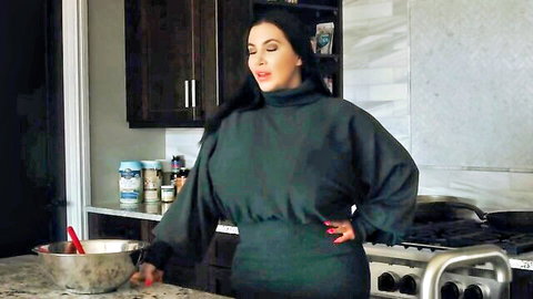 Brunette MILF in tight green turtleneck dress mixing batter in kitchen teasing big tits and curves
