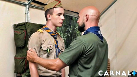Young scout in uniform touched by bald leader in tent, gay intimate moment